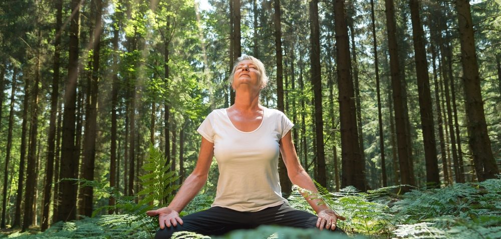 Experience-the-forest-while-bathing-in-the-forest-Shinrin-Yoku-with-all-senses.-A-50-year-old-blonde-woman-sits-cross-legged-relaxed.jpg